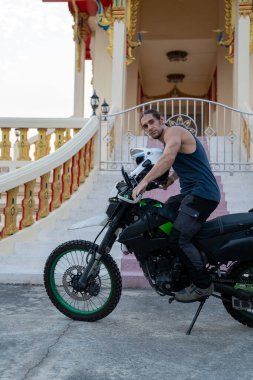 Arka planda miğfer ve tapınak olan motosikletli bir adam macera ve turizmi temsil ediyor.