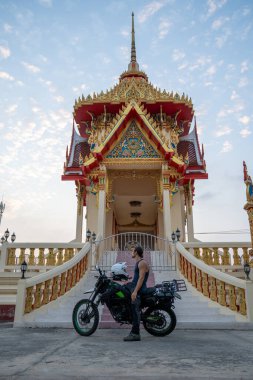 Motosikletli bir adam Tayland 'daki Budist tapınağını ziyaret ediyor.