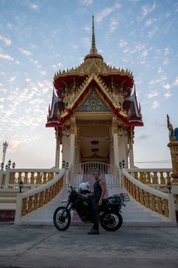 Motosikletli bir adam Tayland Budist tapınağını keşfediyor.