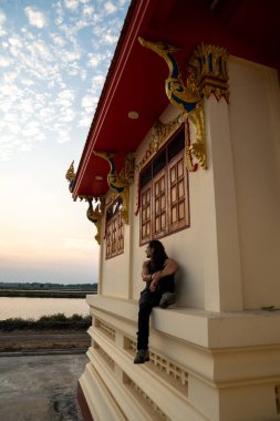 Adam dingin günbatımını izlerken geleneksel bir tapınak binasında dinleniyor.