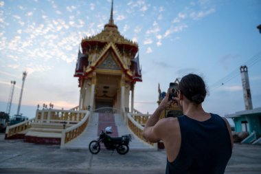 Geleneksel tapınak binasını akıllı bir telefonla fotoğraflayan turist, güzel bir gün batımı sahnesi çekiyor.