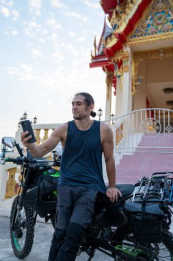 Akıllı telefonlu bir selfie çeken bir adam, tapınağın önünde motosikletin yanında duruyor.