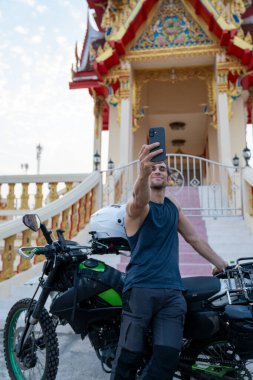 Tayland tapınağının önünde motosikletiyle selfie çeken bir adam.