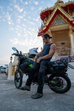 Macera gezisinde olan erkek motosikletçi Tayland 'da bir Budist tapınağının yakınında mola veriyor.