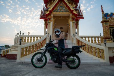 Motosikletli bir adam gün batımında Budist tapınağına gidiyor.