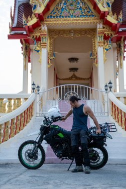 Macera motosikletli bir adam süslü bir Budist tapınağının önünde duruyor.