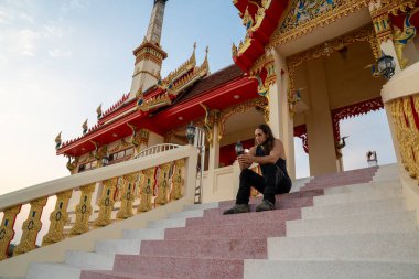 İnsan renkli bir Thai tapınağının merdivenlerinde dinleniyor, ruhani yolculuğunu yansıtıyor.