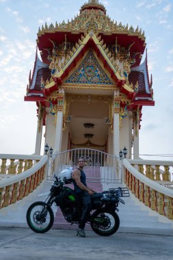 Motosikletli bir adam süslü bir Budist tapınağının önüne park etmiş.