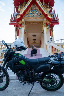 Macera motosikletli bir adam Tayland 'daki bir Budist tapınağının merdivenlerinde dinleniyor.