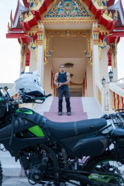 Tayland tapınağının önünde motosikletiyle duran bir adam.
