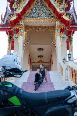 Bir Budist tapınağının merdivenlerinde motosiklet kasklı bir adam dinleniyor.