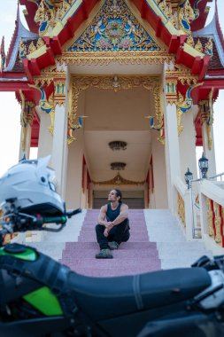 Tapınağın merdivenlerinde oturan, ön planda motosikletli bir adam var.