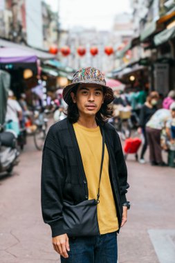 Arka planda bulanık insanlar ve dükkanlarla sokakta poz veren sıradan bir Asyalı.