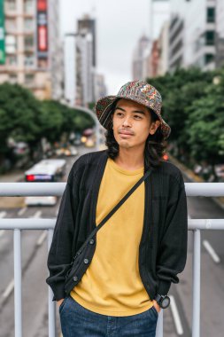 Şehir köprüsünde duran Asyalı genç adam şehir çevresini düşünüyor.