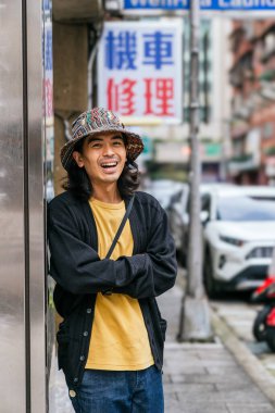 Şehir ortamında gülümseyen desenli bir şapka ve günlük kıyafetler giyen genç bir adam.