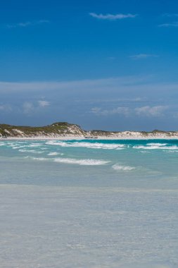 Turkuaz okyanus dalgaları el değmemiş beyaz kumsalları ve mavi gökyüzünün altındaki kumulları yıkıyor.