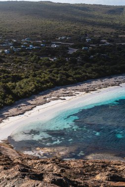 Lucky Körfezi 'nin sakin kıyı şeridi. Beyaz kum, turkuaz su ve uzak bir kamp alanı var.
