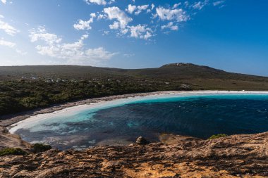 Beyaz kum, berrak mavi su ve güneşli bir gökyüzünün altında engebeli manzaraya sahip güzel sahil şeridi.