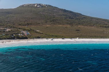 Lucky Bay plajı turist araçlarını ve kristal berrak suyun ve beyaz kumların tadını çıkaran insanları gösteriyor.