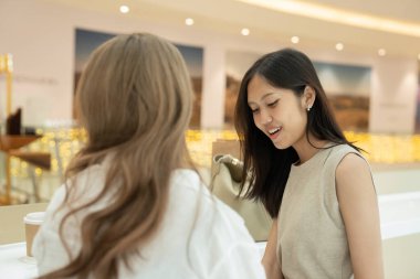 Alışveriş merkezinde rahatlarken neşeli sohbetler yapan iki genç kadın.