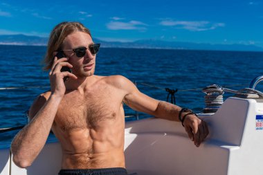 Yatta üstsüz yatarken telefonu kulağına dayayan genç bir adam.