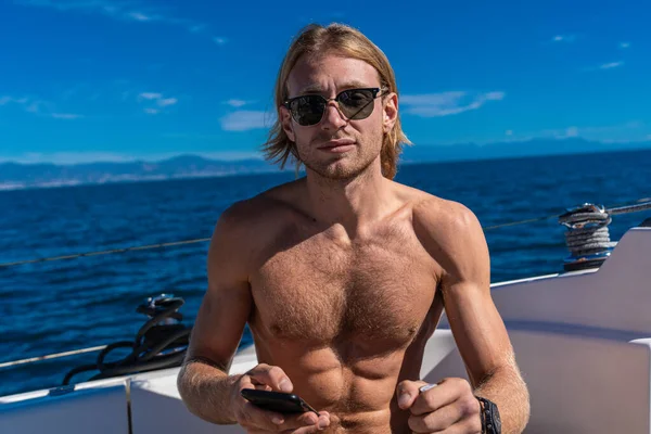 Yaz tatili sırasında yelkenlide telefon kullanan güneş gözlüklü bir adam.