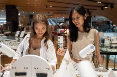 İki Asyalı genç bayan bir mağazada alışveriş yaparken mücevher eşyasına bakıyorlar.