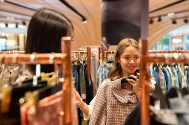 Giyim mağazasında aynaya bakan genç bir kadın ceketini deniyor.