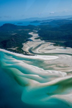 Havadan bakıldığında, tepenin girişinde turkuaz su desenleriyle karışan el değmemiş beyaz silis kumları görülüyor.