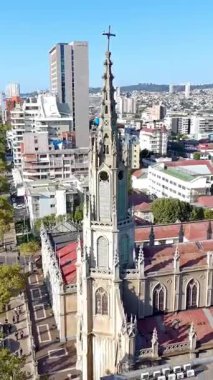 Güneşli bir günde modern bir sahil şehrinin üzerinde yükselen gotik bir kilise kulesinin dikey drone görüntüsü. Iglesia Las Carmelitas, Şili 'de çekildi..