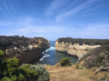 Port Campbell Ulusal Parkı, Victoria, Avustralya - 26 Aralık 2018 - İki kumtaşı kayalığı, açık gökyüzü altındaki çalılar ve toprak yollarla çevrili, derin mavi körfezi çerçeveler.