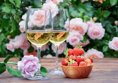 İki kadeh beyaz şarap, güller ve taze çilek ile romantik bir hayat.