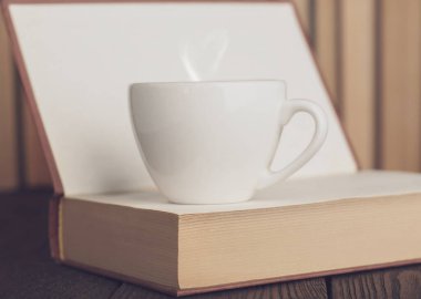 Açık kitap üzerine beyaz kahve fincanı, rahat sabah okuma konsepti.