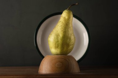 Ahşap bir tezgahta armut ile hayat, arkasında bir tabak ile çerçevelenmiş, yumuşak yeşil bir arka plan.