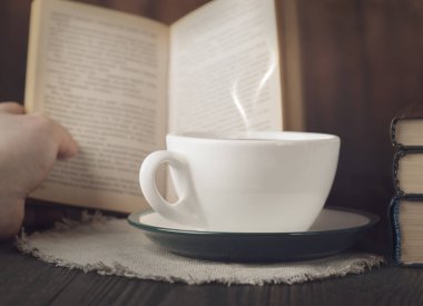 Sıcak kahve, açık kitap ve kırsal ahşap masada buhar ile samimi bir okuma sahnesi.