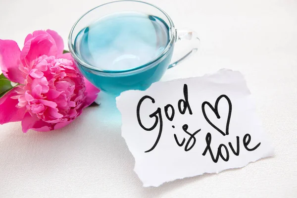 神は愛です クリスチャンの引用 聖書のフレーズと青いお茶とピンクの牡丹の花 — ストック写真