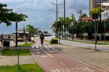 Santos, SP, Brezilya - 17 Ocak 2026: Ponta da Praia 'da bisiklet yolunda bisiklete binen bisikletçiler ve güzel bir cumartesi yazı geçiren insanlar.