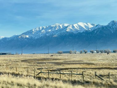 Bu görüntü görkemli bir dağ sırası olan panoramik bir manzara. Ön planda yol kenarının bir kısmını ve kuru, altın renkli otların olduğu bir alanı görebilirsiniz. Ortasında ender bulunan bir bitki örtüsüyle açık bir düzlük var. Dağlar muhteşem görünüyor. !!!