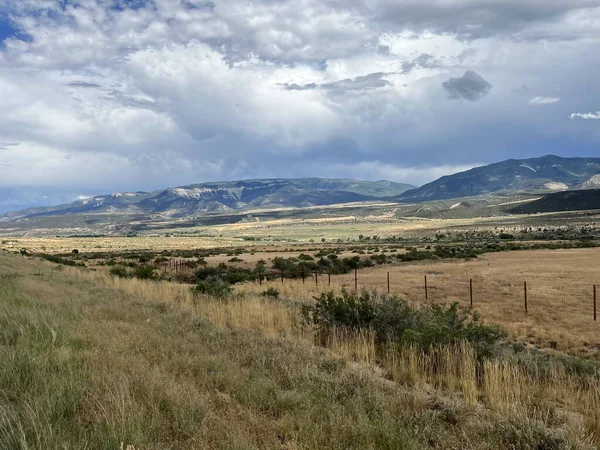 Bulutlu bir gökyüzünün altındaki kayalık bir bölgeden geçen bir yolun fotoğrafı. Sağ tarafta büyük katmanlı kumtaşı bir kaya yükselir ve gri gökyüzü yumuşak, hatta aydınlık yaratarak kanyonun sert güzelliğini vurgular..
