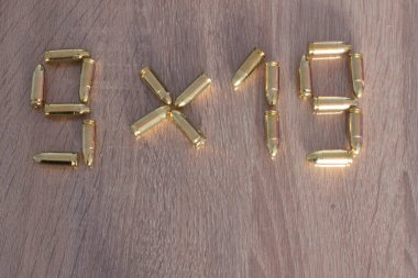 Pirinç mermilerin ahşap arka planda 9x19 kelimelerle yazılması yaratıcı bir düzenleme. Stok fotoğrafçılığı, editör tasarımı ve sanatsal natürmort içeriği için mükemmel..