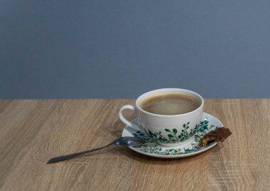 Gövde üzerinde botanik yaprak desenli ve tahta masada koyu metal kaşık olan mükemmel bir kahve fincanı. Kahve dükkanları, kafeler ve içecek pazarlama için profesyonel yemek fotoğrafçılığı. Doğal mavi arka planlı sabah kahve molası kavramı.