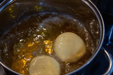 Yakın çekim çiğ hamur topları fırında kaynayan sıcak yağsız tencerede kızarıyor. Yükselen baloncuklu erken kızartma aşaması, pczki tarifleri için mükemmel, fırın dersleri, Şişman Perşembe hazırlığı, geleneksel Polonya hamur işi süreci, yemek tasarımı.