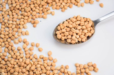 Beyaz arka planda kurumuş nohutlarla dolu metal kaşık, dağınık baklagiller bir çerçeve oluşturuyor, tarif ve beslenme kavramları için kopya alanı olan temiz bir daire çiziyor..