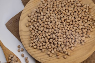 Tahta tabakta kurutulmuş nohut, çuval bezi ve beyaz arka planda tahta kaşık. Rustik yemek malzemesi..