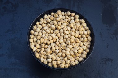 Koyu mavi arka planda siyah bir kasede pişmemiş kuru nohut manzarası. Huysuz, modern yemek..