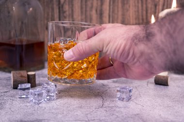 El ele tutuşmuş kristal bir bardak viski ve buzlu arka planda bir şişe. Klasik ruhlar ve bar konsepti.