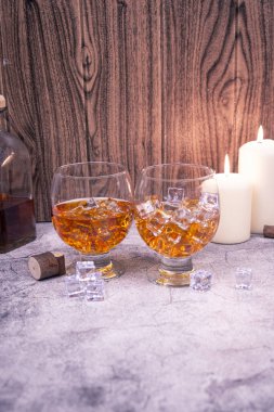 Buzlu, biberonlu ve mumlu iki viski kadehiyle dikey köy sahnesi. Çubuk, bağımlılık veya uyarı mesajı için bir sürü kopya alanı.