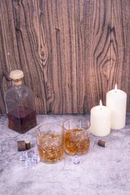 Buzlu iki viski bardağı, şişe ve mumlarla tahta bir arka planda dikey bir hayat. Reklamlar, menüler, gece hayatı ya da alkolizm farkındalığı için bolca kopya alanı var..