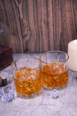 Taş bir masada buzlu iki viski bardağı, kırsal şişe ve mum ışığı arka planı. Konforlu çubuk sabit hayat, dikey kompozisyon.