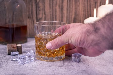 Elleri, üzerinde buz küpleri olan bir viski bardağına uzanır. Mum ışığında kırsal bir zeminde. Baştan çıkarma, gece yarısı içkisi, bağımlılık ya da alkolizm kavramı.